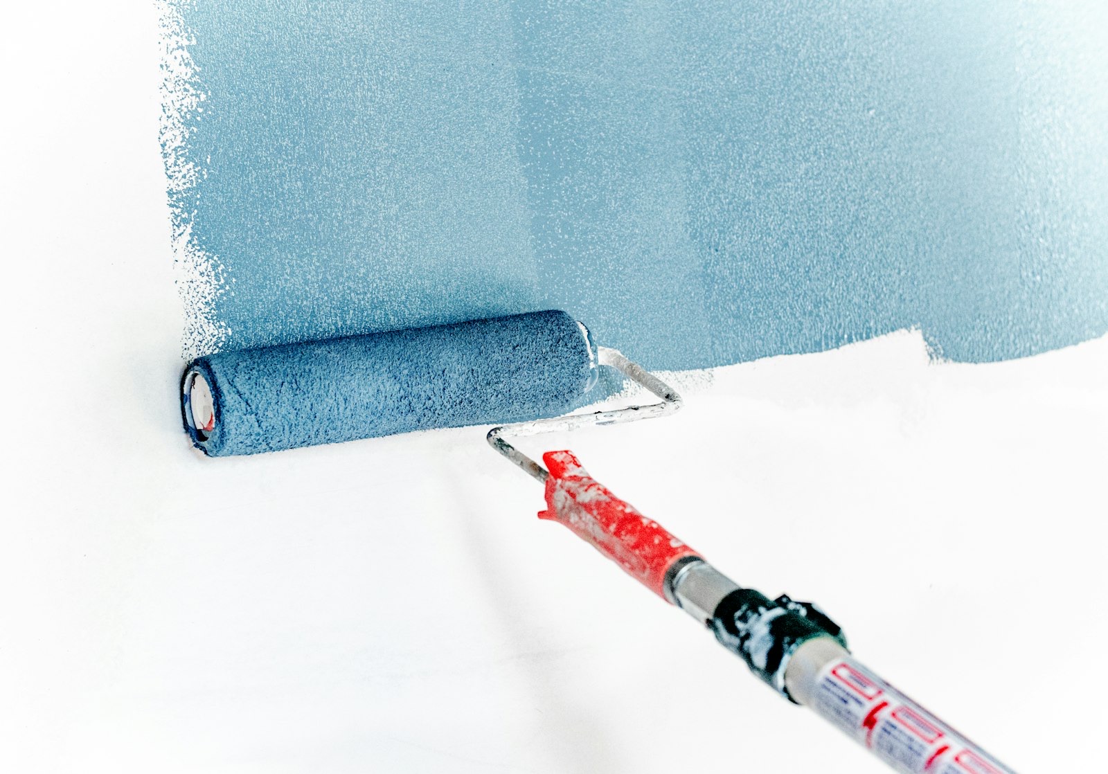 A paint roller spreading soft blue paint across a white interior wall